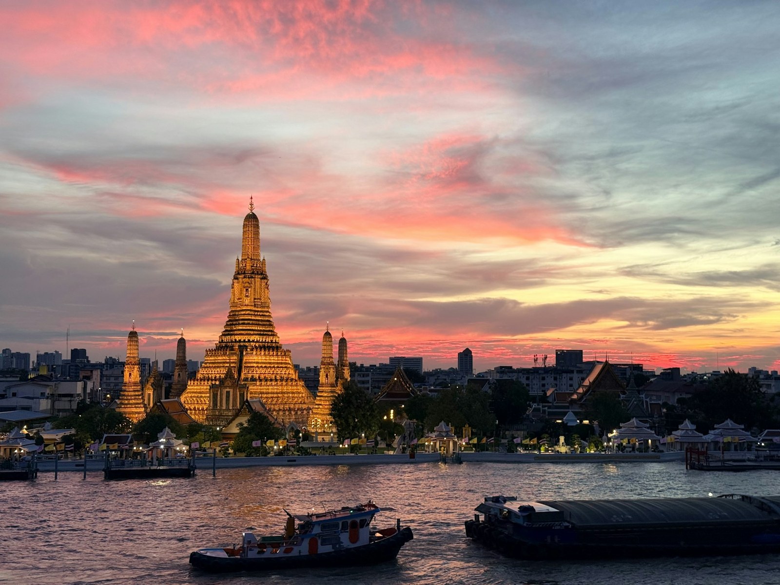 Il tempio Wat Arun illuminato oltre il fiume Chao Phraya sotto un cielo colorato
